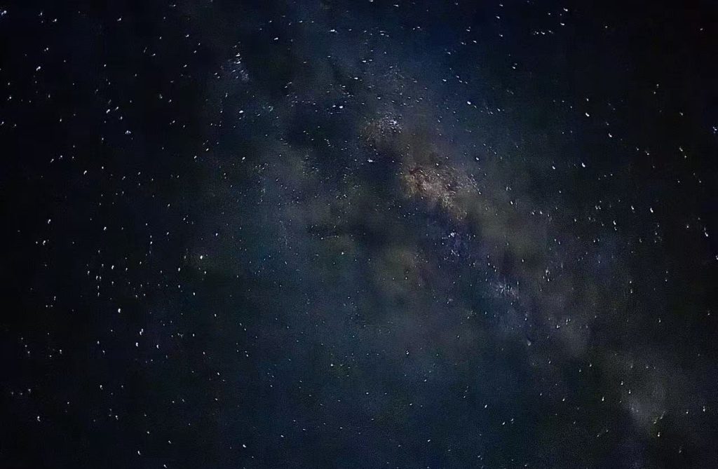 In the pitch-black night sky, stars are scattered like spilled white paint, with a diagonal purple Milky Way cutting through the middle.